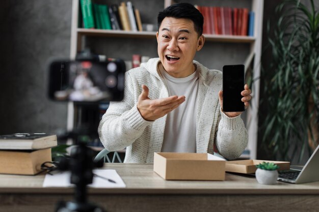 Angenehmer asiatischer Mann öffnet Paketbox mit neuem Smartphone