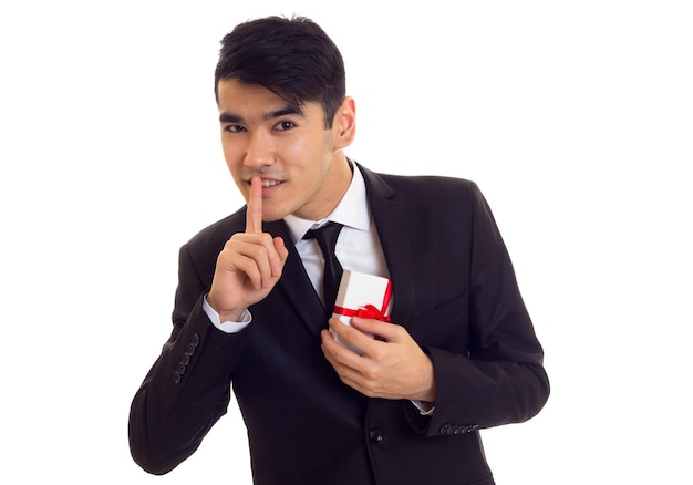 Angenehmer Mann mit schwarzen Haaren in weißem Hemd und schwarzem Smoking mit schwarzer Krawatte, die ein Geschenk hält