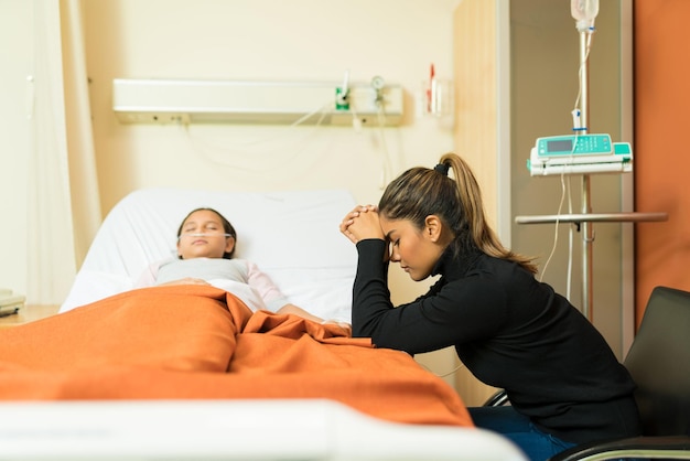 Foto angespannte mutter sitzt neben bewusstloser tochter, die im krankenhaus auf dem bett liegt