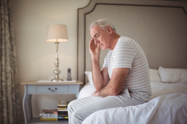 Angespannter Mann, der auf Bett im Schlafzimmer sitzt