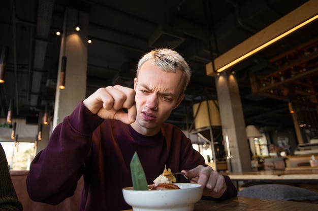 Angewiderter junger Mann fand Haare in seiner Mahlzeit im Café und sieht sie mit Abscheu an