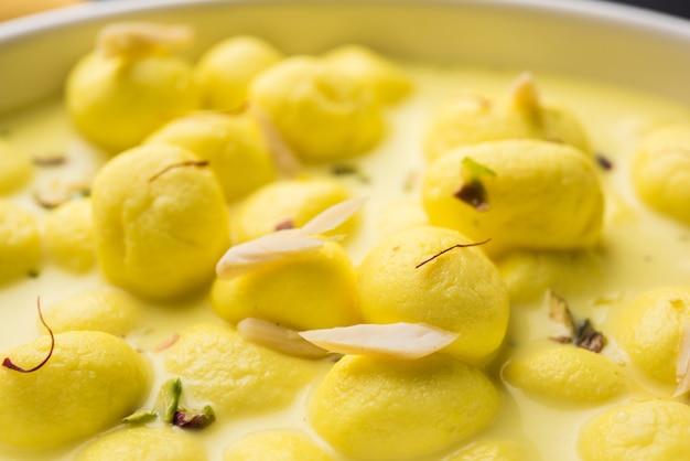 Angoori Rasmalai é uma sobremesa indiana doce com frutas secas e coberturas de açafrão, servida em uma tigela sobre um fundo melancólico. foco seletivo