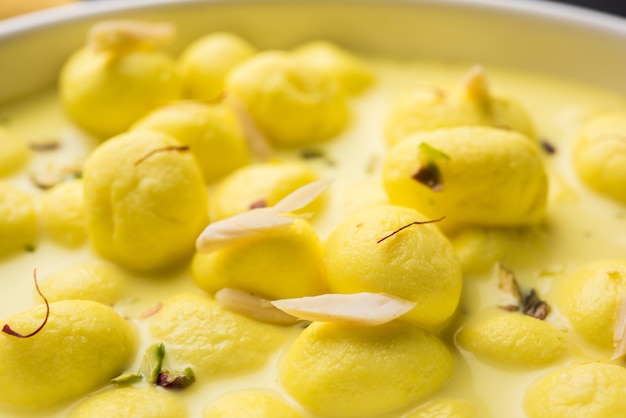 Angoori rasmalai é uma sobremesa indiana doce com frutas secas e coberturas de açafrão, servida em uma tigela sobre um fundo melancólico. foco seletivo