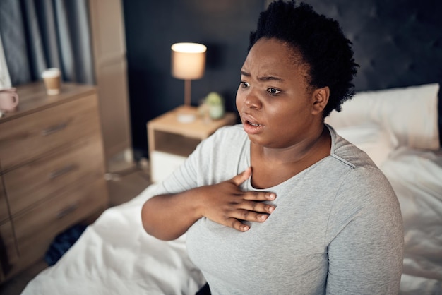 Angst im Schlafzimmer und eine schwarze Frau mit einem Angstanfall oder Schmerzen in der Brust aufgrund von Stress. Beängstigende Gesundheit und ein afrikanisches Mädchen auf einem Bett mit Panikdepression oder einem psychischen Fehler oder krank für die Psychologie