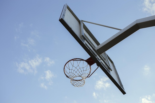 Ángulo bajo del aro de baloncesto con red y tablero contra el cielo azul en la cancha urbana de la ciudad