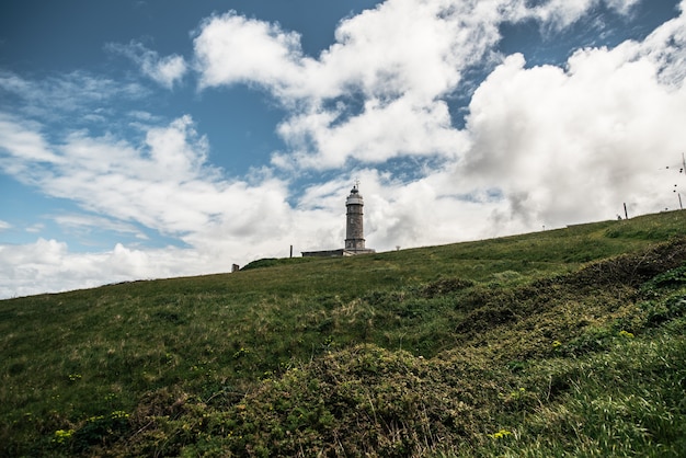 ângulo baixo do antigo farol do prefeito faro de cabo localizado em uma colina gramada contra o céu azul nublado