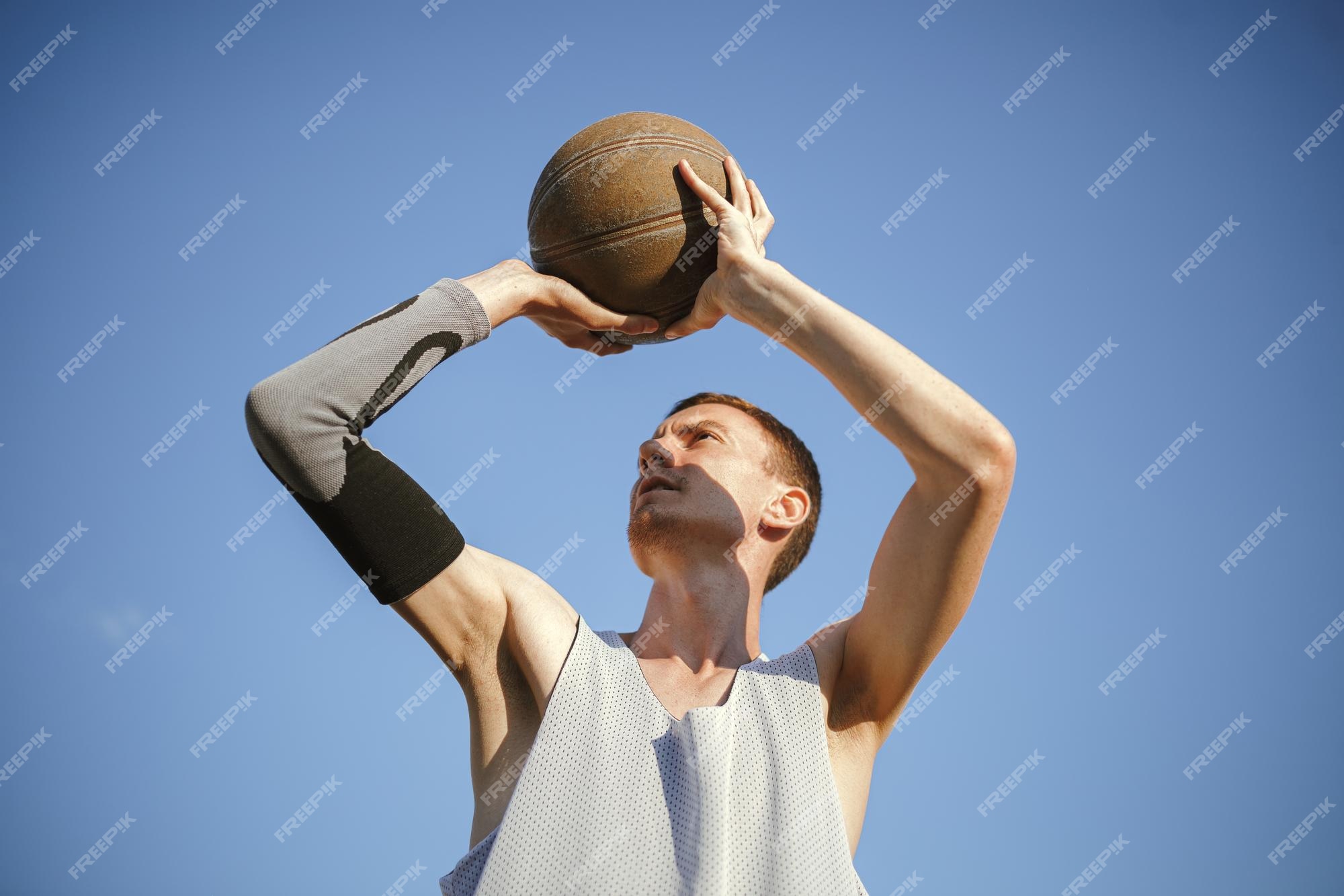 Ângulo baixo do jogador de streetball masculino mirando com bola enquanto  jogava basquete contra o céu azul