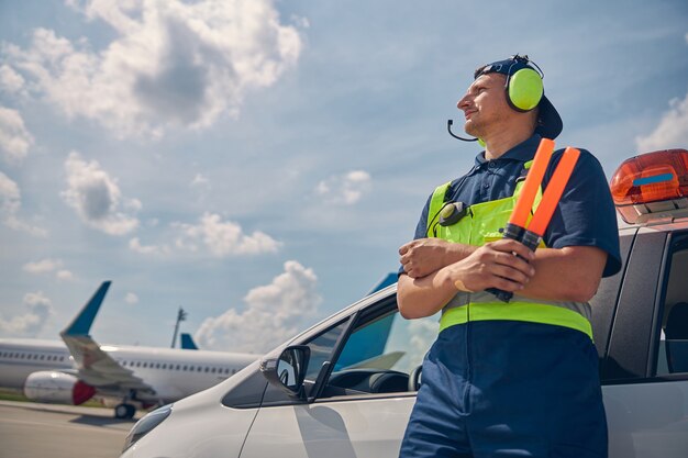 Ángulo bajo de un trabajador del aeropuerto caucásico enfocado con varitas de clasificación mirando a la distancia