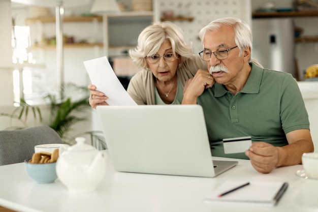 Angustiada pareja de ancianos ebanking con tarjeta de crédito y computadora portátil en casa