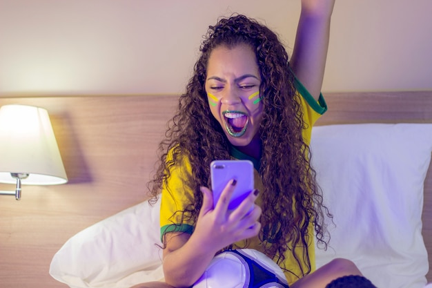 Anhänger der brasilianischen Fußballmannschaft, die ein Ziel feiert, indem sie das Smartphone ansieht