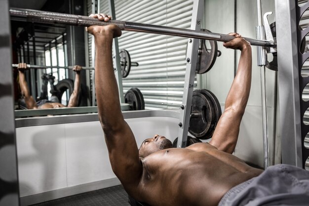 Anhebender Barbell des hemdlosen Mannes auf Bank an der crossfit Turnhalle