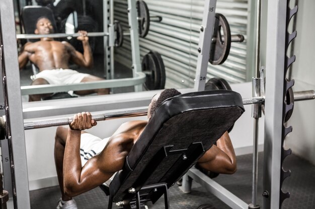 Anhebender Barbell des hemdlosen Mannes auf Bank an der crossfit Turnhalle