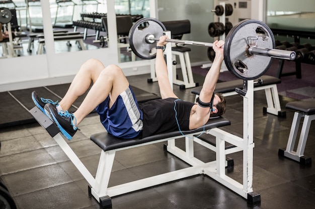 Anhebender Barbell des muskulösen Mannes auf Bank an der Turnhalle