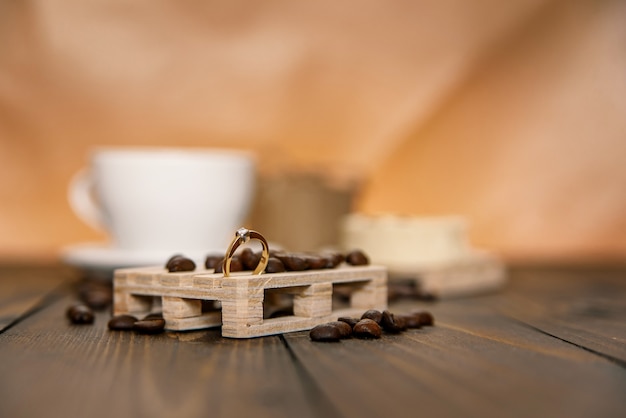 Anillo de compromiso de diamantes en el soporte de madera con granos de café y una taza de café con pastel