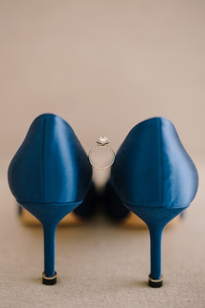 Anillo de compromiso de novias con una gema entre zapatos de tacón azul en el suelo sobre un fondo beige