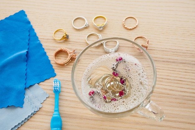 Anillo de diamantes de joyería de limpieza con un vaso de agua caliente y líquido para lavar platos en la mesa de madera