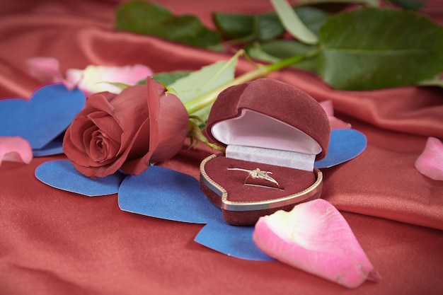 Anillo de diamantes y rosa sobre fondo rojo brillante