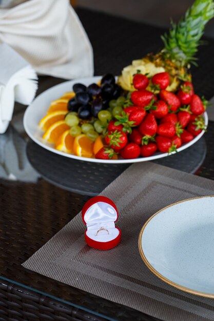 Anillo de joyería preciosa de oro de compromiso para una niña en un cuadro rojo sobre un fondo de fruta