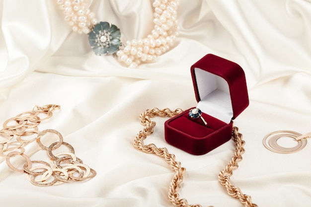 Anillo de oro con diamante en caja de regalo roja y otras joyas sobre tela de seda