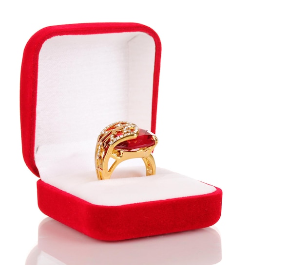 Anillo de oro con una gran gema roja y cristales transparentes en una caja de terciopelo rojo aislada en blanco