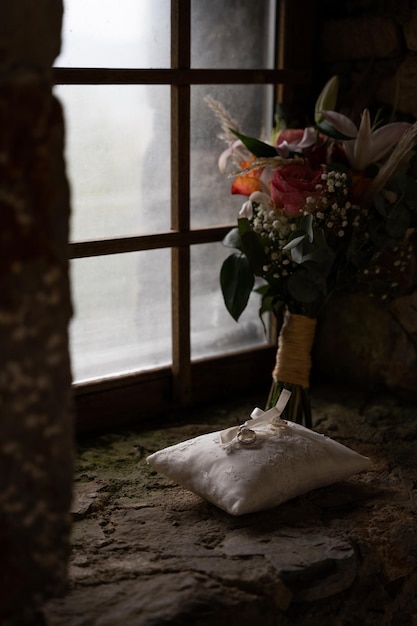 anillos de boda en una almohada, un ramo de flores en el fondo y una ventana, joyas en un día lluvioso