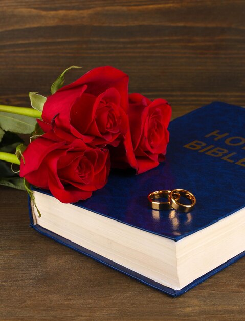 Anillos de boda en la Biblia con rosas sobre fondo de madera