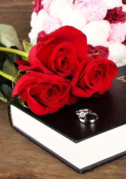 Anillos de boda en la Biblia con rosas sobre fondo de madera