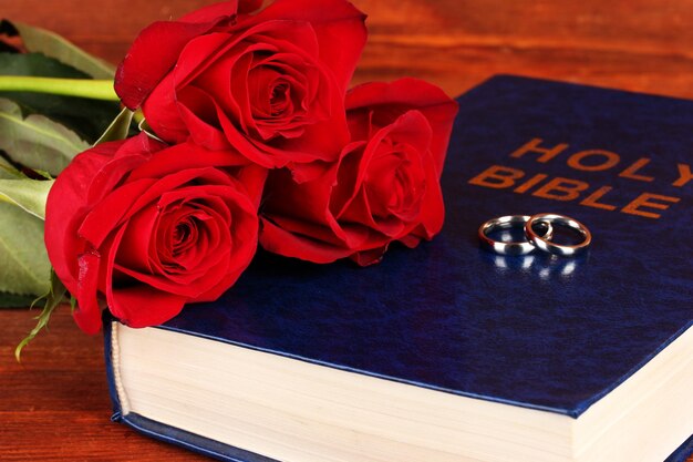 Anillos de boda en la biblia con rosas sobre fondo de madera