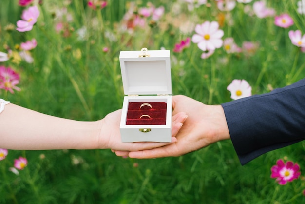 Foto anillos de boda en una caja en las palmas de las manos de la novia y el novio sobre un fondo de flores