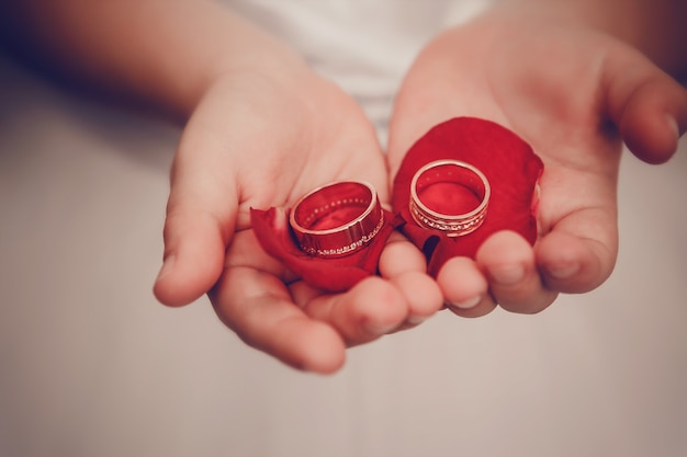 Los anillos de boda se encuentran en las palmas de los niños con pétalos de rosas