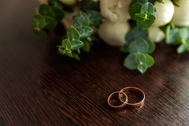 Los anillos de boda se encuentran en la superficie de madera contra el fondo del ramo de flores
