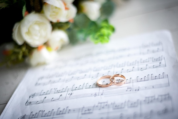 Anillos de boda en el fondo de la notación musical y ramo de bodasxA