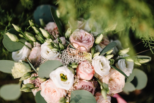 Anillos de boda novia y novio en el ramo de novia de fondo con flores y rosas blancas y vegetación sobre la hierba