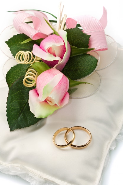anillos de boda de oro en la almohada blanca con rosa