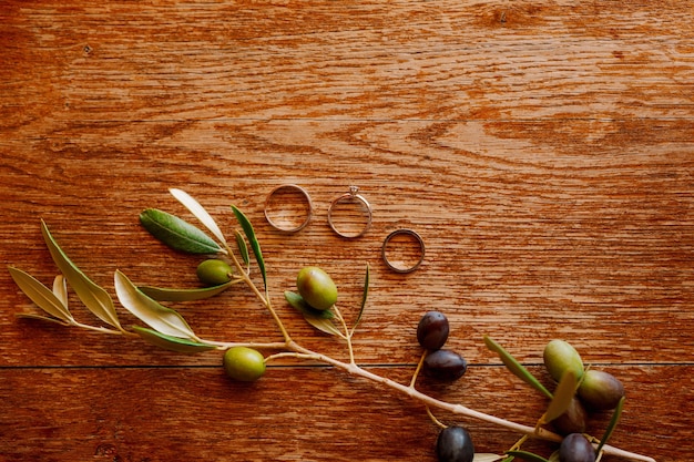 Anillos de boda de oro y un anillo de compromiso sobre un fondo marrón con una ramita de frutos de olivo