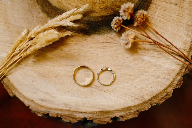 Anillos de boda de oro en un corte de madera con espiguillas y flores secas