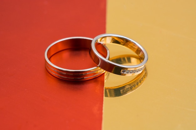 Foto anillos de boda de oro sobre una superficie roja y dorada.