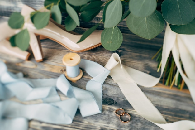 Foto anillos de boda de oro con zapatos beige de la novia y un carrete con cinta sobre una superficie de color verde