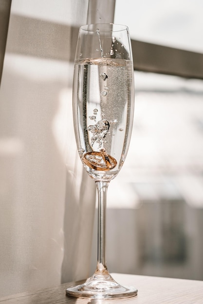 Anillos de boda que se hunden en agua en gotas de burbujas de agua de vidrio El conjunto de anillos de compromiso Hermoso fondo dorado con anillos de novio y novia