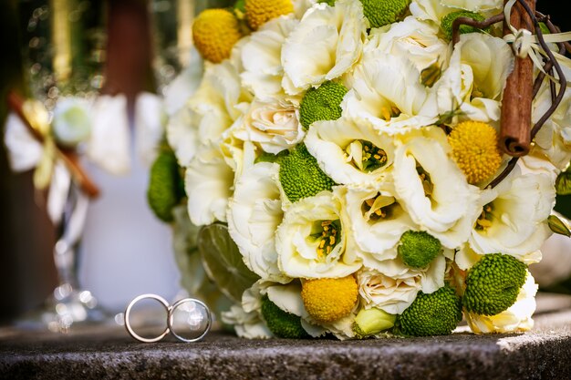 Anillos de boda con ramo de rosas beige, canela, limón, lima y copas de champán.