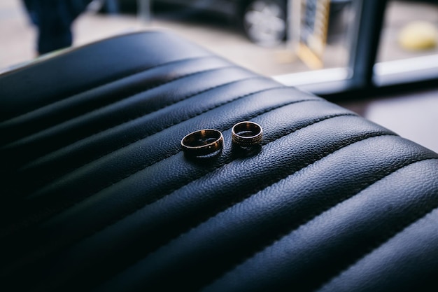 anillos de boda de los recién casados yacen en la silla de peluquero en la barbería, fondo oscuro de cuero