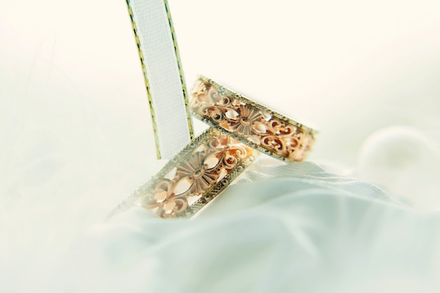 Anillos de boda de la vendimia entre las cintas blancas, primer. anillos de oro con patrones sobre un fondo blanco borroso. boda y tradiciones familiares.