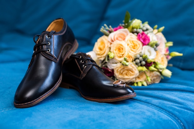 Los anillos de boda de los zapatos de los hombres se encuentran en los zapatos de los hombres, junto a un hermoso ramo de novia