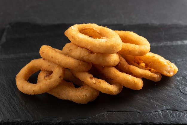 Anillos de calamar fritos en anillos de calamar crujientes empanados sobre un fondo oscuro con salsa