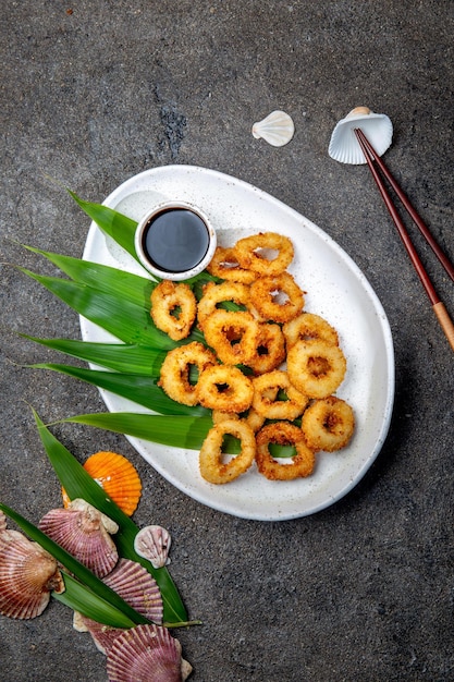 Anillos de calamares fritos en un plato blanco decorado con hojas tropicales vista superior de fondo de hormigón gris