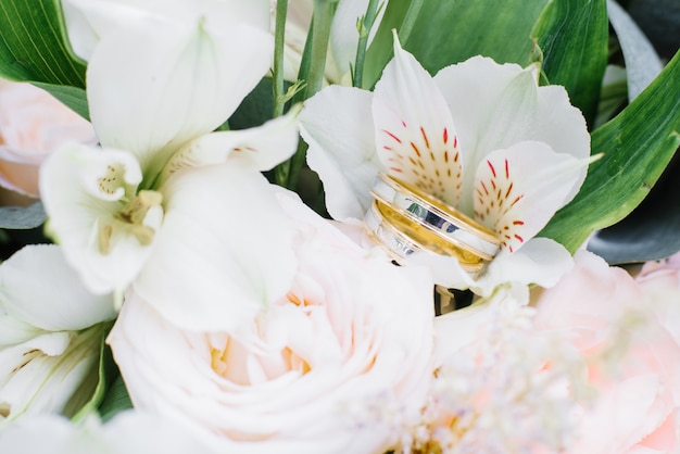 Los anillos de compromiso de boda de oro amarillo y blanco están en el ramo de la boda.