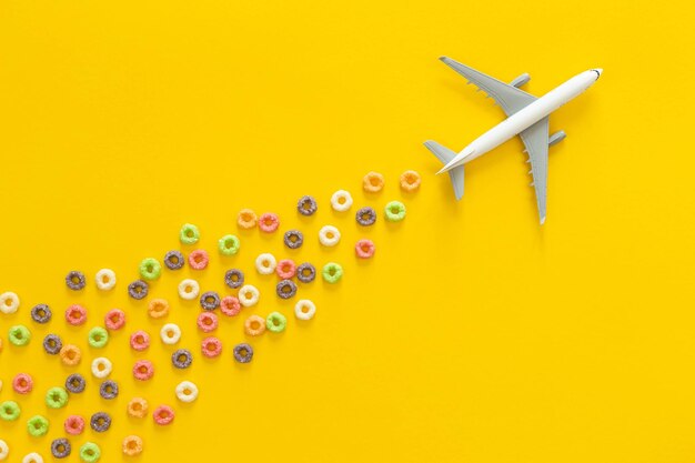 Anillos de maíz de frutas coloridas y avión de juguete en un fondo plano amarillo