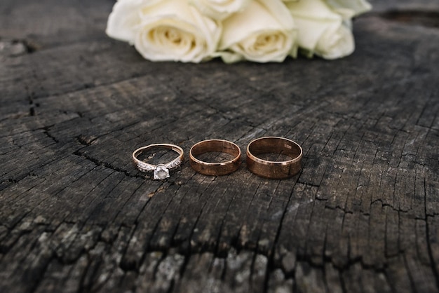 Foto anillos de oro de boda con diamantes y ramo de rosas blancas en el fondo de madera