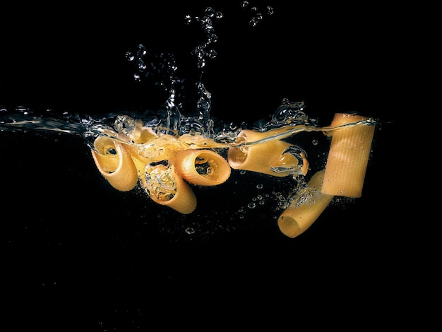 Foto anillos de pasta cayendo en el agua hirviendo sobre fondo oscuro vista submarina