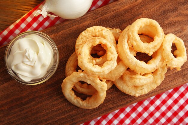 Anillos de patatas fritas con salsa y cebolla en primer plano de la tabla de cortar